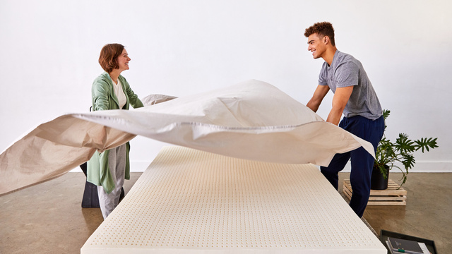 a man and a woman put bedsheets on a mattress